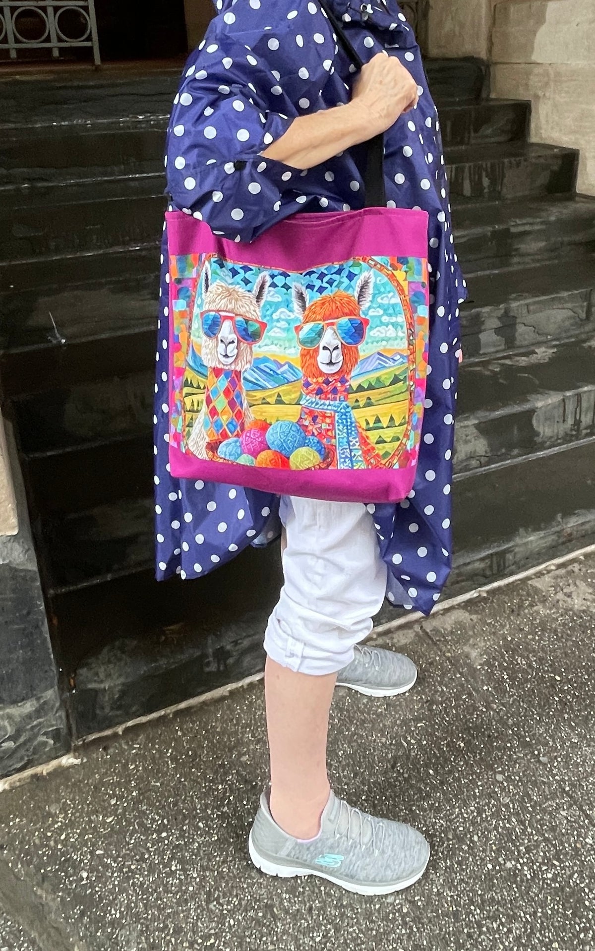 Two Chic Llamas Tote Bag worn over the shoulder in the rain, model in a blue polka dot poncho, no face shown.